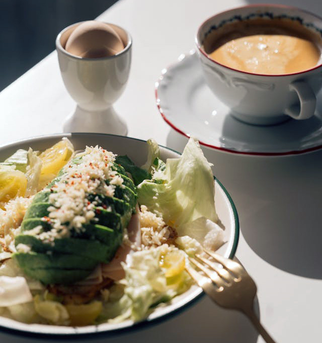 a breakfast table with salad, fresh juice, eggs, fruits, croissants, and a cup of coffee