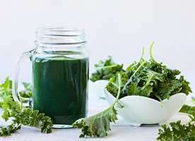 kale smoothie in a mason jar with a bowl of kale and scattered kale leaves on a white table